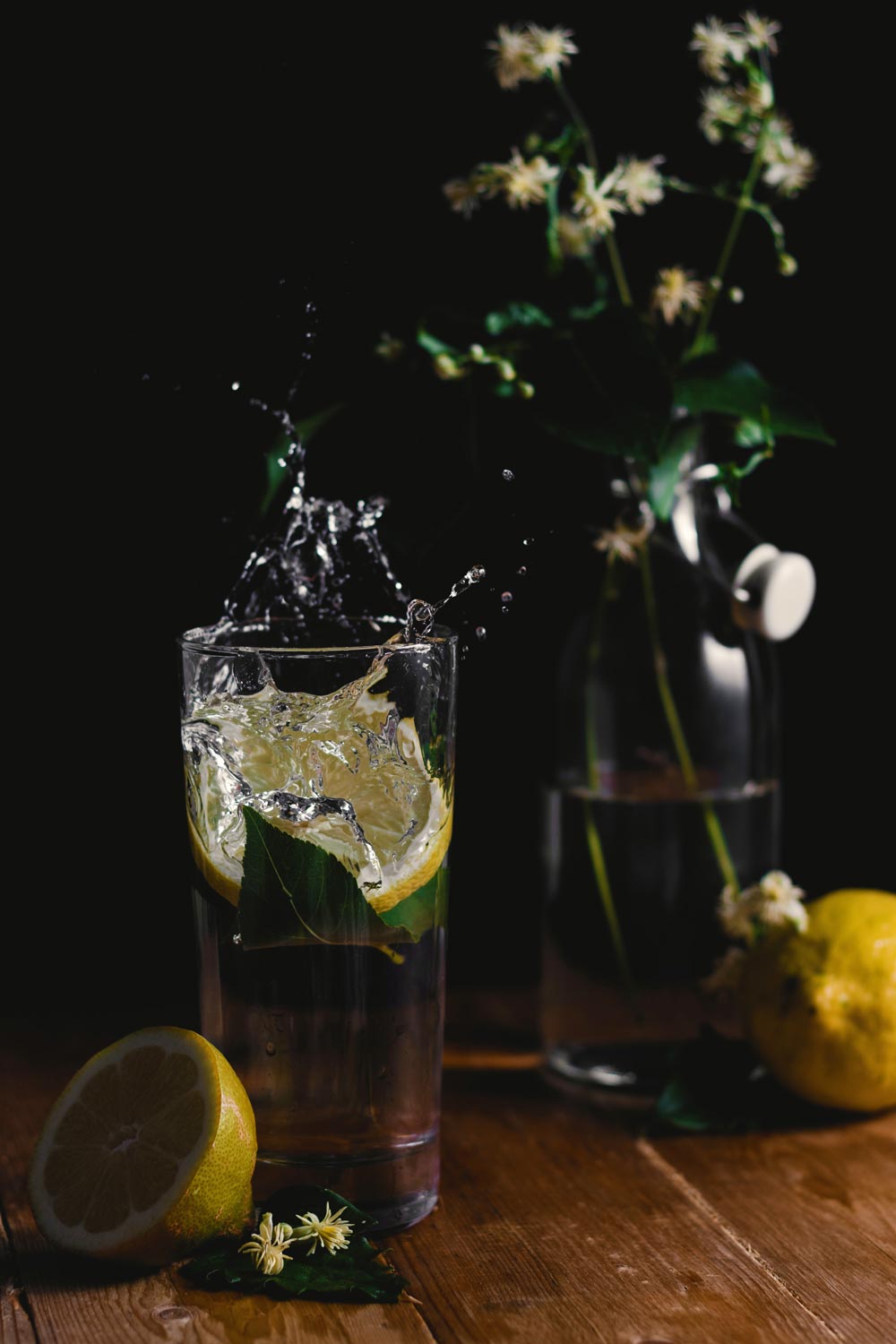 Glass of water with lemon slices and flowers on a wooden table